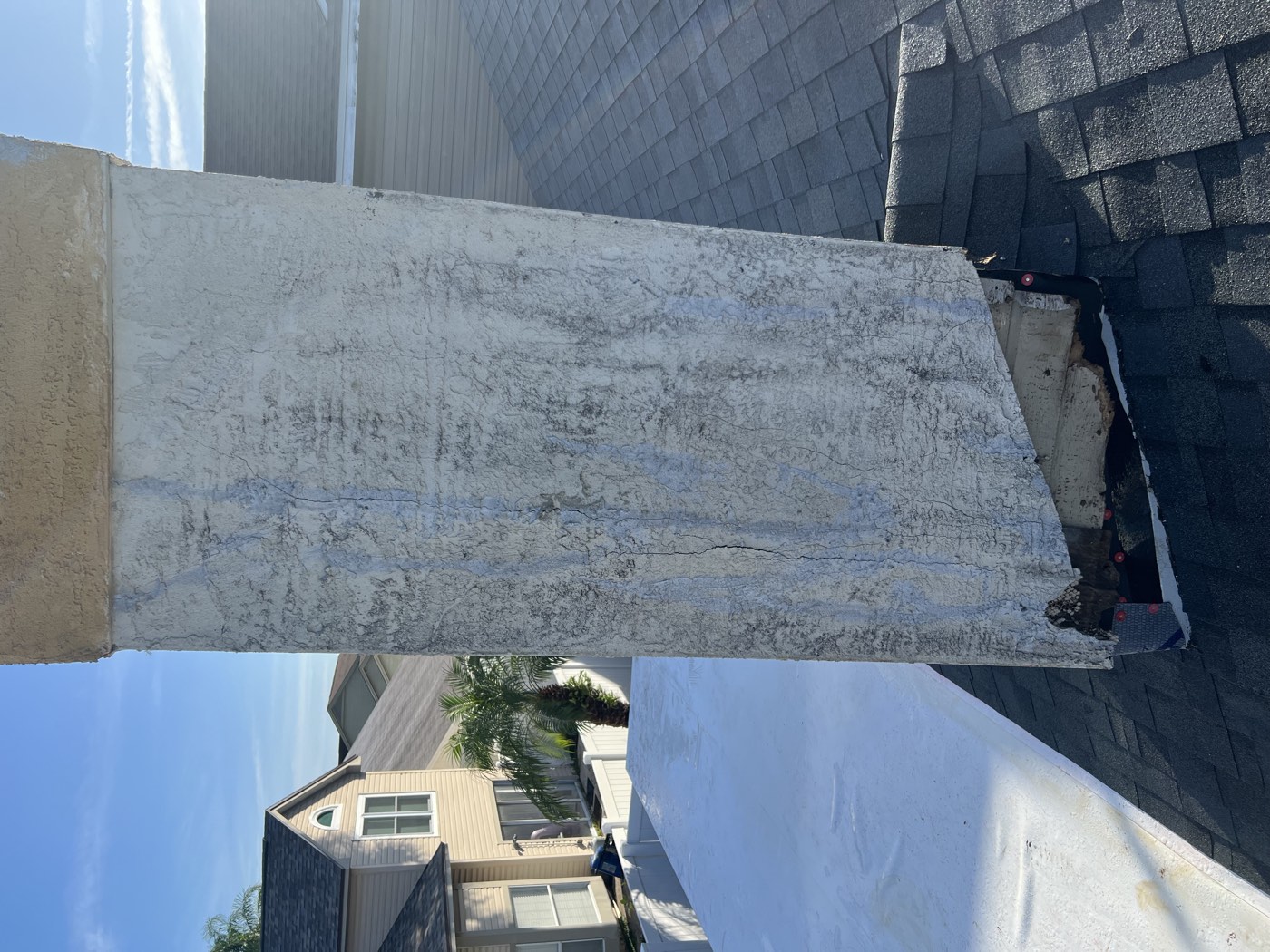 A chimney with cracked, stained stucco and a damaged base